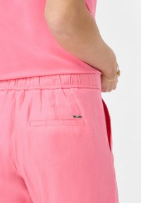 Roze elastische broeken met een achterzak. Zachte stofstructuur, minimalistisch ontwerp en een klein merkje naast de zak.