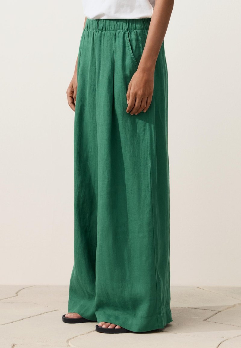 Persona che indossa pantaloni verdi larghi e morbidi con vita elastica e tasche laterali, abbinati a sandali neri.