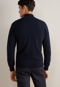 Mörkblå stickad tröja med hög krage, ribbade ärmmuddar och nederkant. Mjuk textur med en åtsittande silhuett, minimalistisk design, inga synliga mönster.