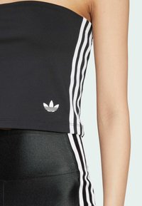 Čierny top bez ramienok s bielymi prúžkami a malým logom Adidas na spodnom leme. Hladká textúra látky.