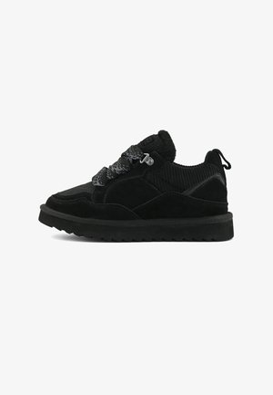 Sneaker nera in suede e tessuto con suola spessa, lacci texturizzati, collare imbottito e linguetta sul tallone, mostrata dal lato esterno.