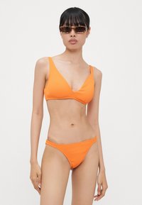 Ensemble de bikini côtelé orange vif comprenant un haut en V et un bas taille basse assorti, mettant en avant une texture lisse et un design minimaliste.