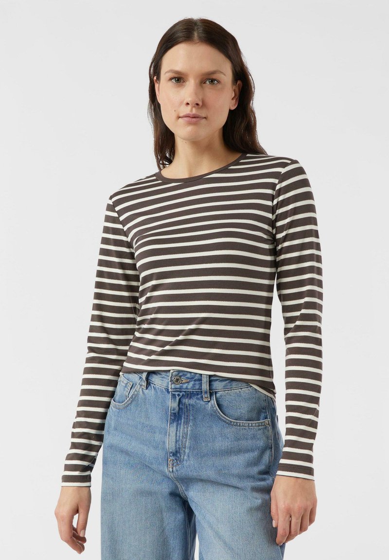 Koszula w paski z długim rękawem w ciemnym brązie i kremowym kolorze. Posiada okrągły dekolt. Połączona z jasnoniebieskimi dżinsami. Gładka faktura tkaniny.