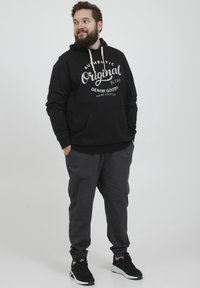 Sudadera negra con el texto "Authentic Original Blend Denim Goods" en blanco, combinada con pantalones grises. Presenta un bolsillo frontal y capucha con cordón.