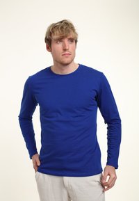 Dlouhý rukáv modré košile z hladkého materiálu s kulatým výstřihem a fitted střihem. Neobsahuje žádné viditelné vzory ani akcenty. Jednoduchý a čistý styl.