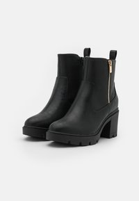 Botas negras hasta el tobillo con un acabado de cuero suave, detalle de cremallera lateral, tacón grueso y suela de goma para mayor tracción. Incluyen tiradores para facilitar el uso.