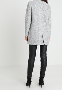Cappotto grigio in tweed con taglio dritto e spacchi posteriori, abbinato a leggings neri in ecopelle e stivali neri alla caviglia.