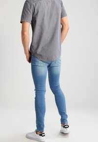 Lichtblauwe skinny jeans van denim, gecombineerd met een kortekraag grijs shirt. Schoenen zijn wit met zwart Nike-logo op de hiel.