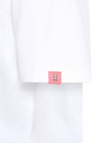 Witte katoenen T-shirt met een klein roze label met een grijs ontwerp van een hond op de mouw. Bekijk een gladde textuur en korte mouwen.