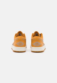 Žluté kožené tenisky s bílou podrážkou, vybavené modrým akcentním pruhem a vyšívaným logem. Zaoblená špička, nízký design a textura gumové podrážky.