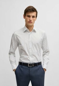 Witte shirt met kleine blauwe vierkantjes, button-up kraag, lange mouwen en een zwarte riem; gedragen met marineblauwe gestructureerde broek.