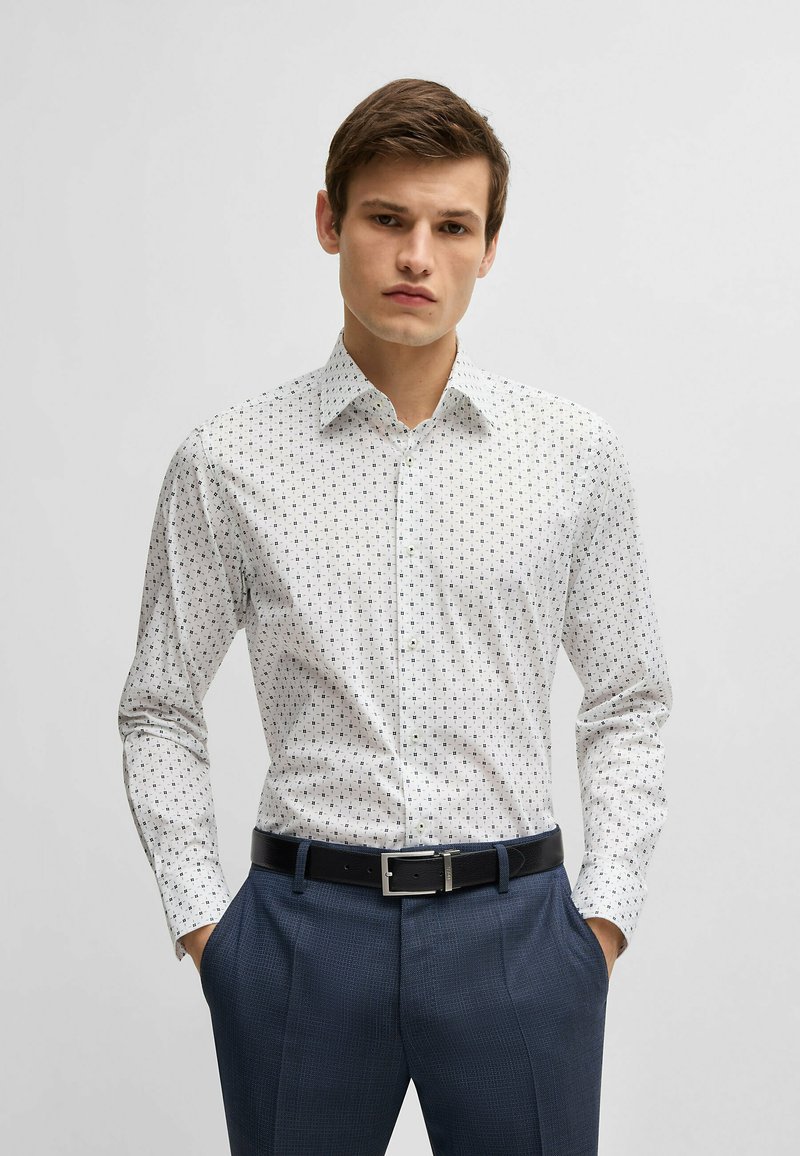 Witte shirt met kleine blauwe vierkantjes, button-up kraag, lange mouwen en een zwarte riem; gedragen met marineblauwe gestructureerde broek.