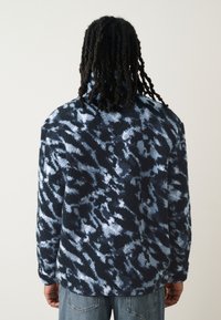 Fleecejack met een abstract patroon in marineblauw en lichtblauw, hoge kraag, lange mouwen en een losse pasvorm, ontworpen voor comfort.