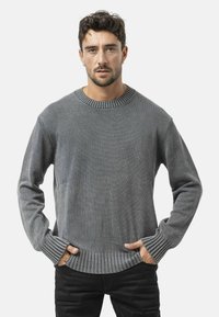 Pull en maille gris avec un col et un ourlet côtelés, à manches longues et à coupe décontractée. La texture du tissu semble douce et légèrement texturée.