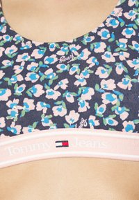 Ziedu bralette ar tumši zilu pamatni, rozā un zilu ziedu dizainu, mīkstu audumu, apaļu dekoltē un rozā logotipa joslu ar uzrakstu "Tommy Jeans."