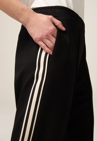 Zwarte sportbroek met witte en zwarte strepen aan de zijkanten. Elastische tailleband, zichtbare zijzak, zachte stofstructuur.