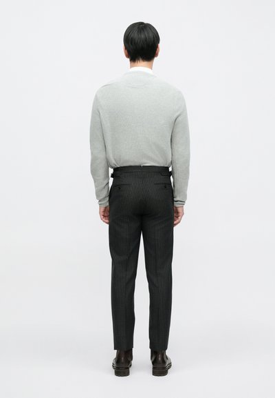 Sivi džemper s okruglim izrezom u kombinaciji s crnim hlačama s tankim prugama. Hlače su krojene po mjeri i imaju džepove. Izgled upotpunjuju smeđe cipele.