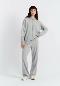 Grauer Hoodie mit einem Frontreißverschluss und Kängurutasche, kombiniert mit passenden lockeren Hose. Glatte Textur, lässiges sportliches Design.