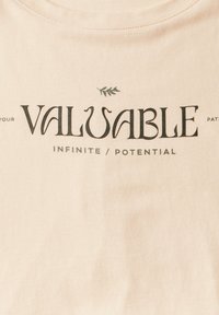Camiseta de algodón color durazno con el texto: "TU POTENCIAL VALIOSO", con un pequeño acento de hoja verde sobre la palabra "VALIOSO".