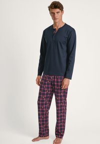 Marineblauw longsleeve shirt met een henley-ontwerp; geruite pyjama's in bordeauxrood, roze en crème met een herhaald patroon van ananassen.