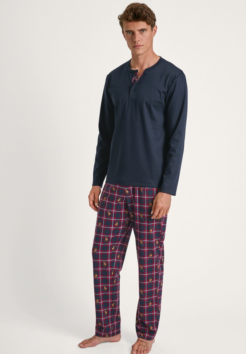Marineblauw longsleeve shirt met een henley-ontwerp; geruite pyjama's in bordeauxrood, roze en crème met een herhaald patroon van ananassen.