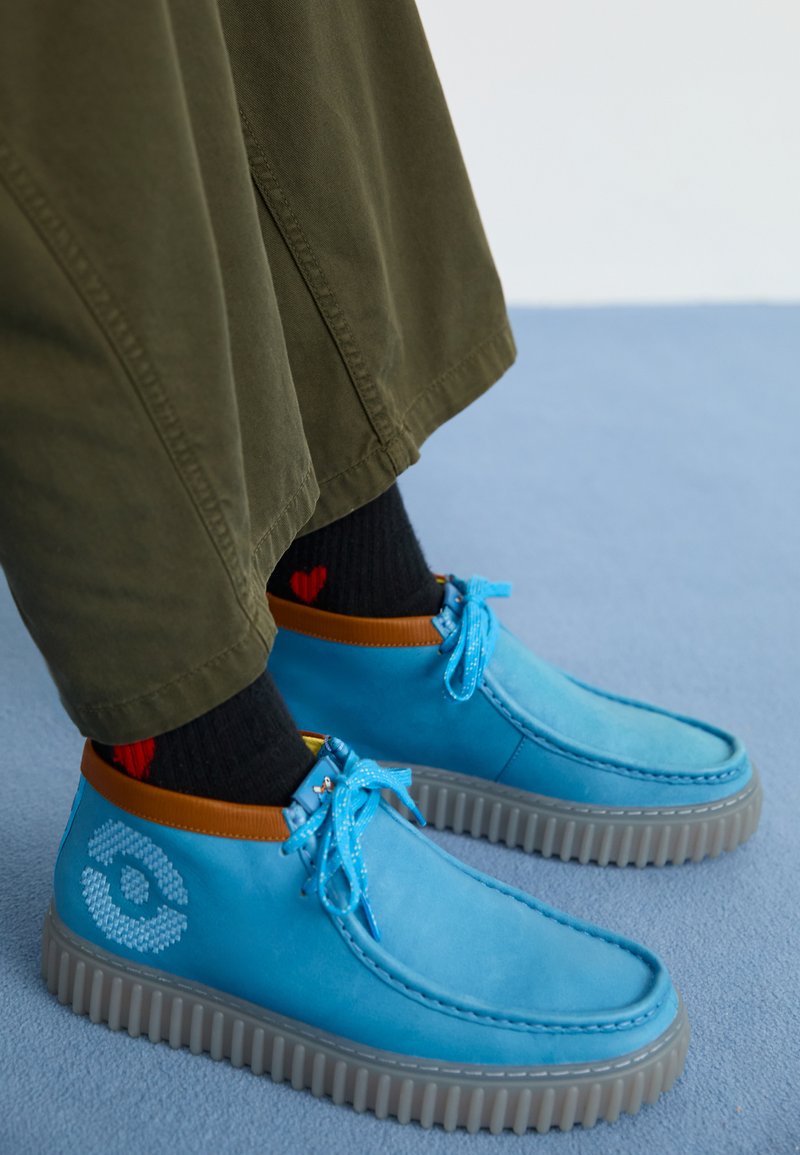 Blue leather shoes with a smooth finish, featuring a tan accent at the collar, rubber sole, and decorative laces. Pairing with black socks.