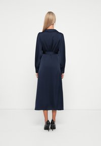 Navy satin dress with long sleeves and a collar, featuring a belted waist and a flowing, midi-length skirt. Worn with black high heels.