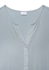 Světle modrá blůza s výstřihem do V, vyrobená z hladké látky. Obsahuje přední zapínání na šest knoflíků a jemné švy.