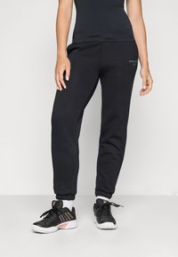 Svarta sweatpants med elastiska muddar, med en mjuk textur och logodetalj. Parat med svarta sportskor med vita sulor och detaljer.