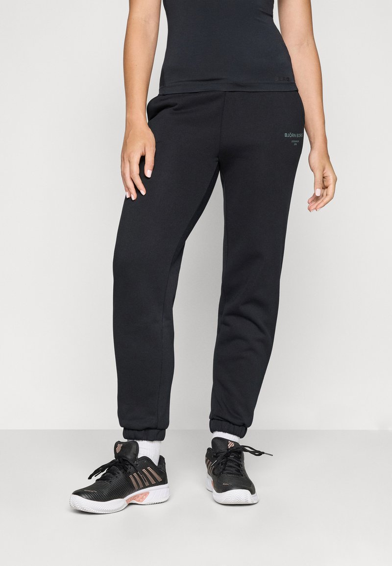 Svarta sweatpants med elastiska muddar, med en mjuk textur och logodetalj. Parat med svarta sportskor med vita sulor och detaljer.