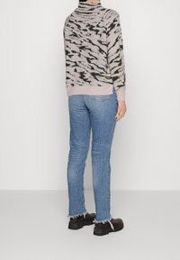 Lichtroze sweater met een donkergroen abstract patroon, raglan mouwen en geribde manchetten. Verbleekte blauwe denim jeans met rafelige zomen en zwarte schoenen.