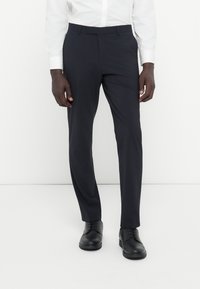 Mornarske hlače iz gladkega blaga s prilagojenim krojem, ravnim sprednjim delom in zankami za pas, v kombinaciji s črnimi čevlji na vezanje.