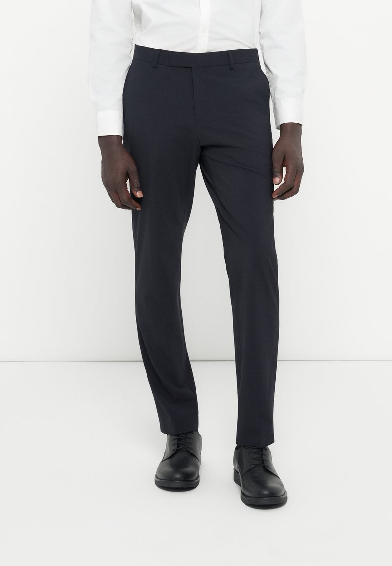 Laivaston siniset puvuntakit sujuvasta kankaasta, joissa on muotonsa mukainen istuvuus, tasainen etuosa ja vyölenkit. Yhdistetty mustiin, nauhoilla sidottuihin kenkiin.