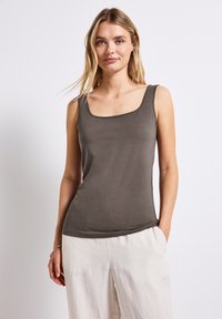 Top grigio aderente senza maniche con scollo quadrato e spalline largh, realizzato in un tessuto morbido. Abbinato a pantaloni larghi di colore chiaro.