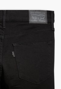 Zwarte denim jeans met een gestructureerd oppervlak. Beschikt over een achterzak met een kenmerkend stikpatroon en een grijs leren merklabel.