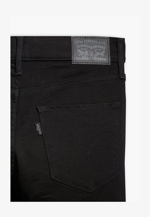 Jeans in denim nero con una superficie strutturata. Presentano una tasca posteriore con un motivo di cucitura distintivo e un'etichetta in pelle grigia del marchio.