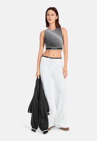 Black and white crop top with polka dots, paired with white, loose-fitting pants and holding a black bomber jacket.