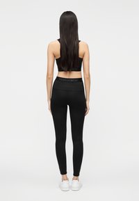 Musta urheilullinen lyhyt paita ja korkeavyötäröiset leggingsit, joissa on sileä pinta ja vähän yksityiskohtia, yhdistettynä valkoisiin lenkkareihin.