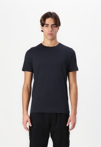 Tums zilā īsām piedurknēm T-kreklā izgatavots no kokvilnas, ar apaļu kakla izgriezumu un regulāru piegriezumu, valkāts kopā ar melnām kargo biksēm.