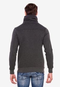 Dunkelgrauer Sweatshirt mit hohem Kragen und Reißverschlussdetail, mit strukturiertem Finish, gerippten Bündchen und Saum, kombiniert mit blauen Jeans.