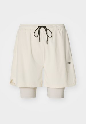 Cremefarvede sportsshorts med elastisk talje, snor og indvendige beige leggings. Tekstureret stof og sideslids for bevægelsesfrihed.