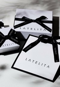 Three white gift boxes with black ribbon featuring "LATELITA" logo. The boxes vary in size, with a smooth finish and contrasting black accents.