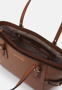 Ruskea nahkainen käsilaukku, jossa on kultaiset yksityiskohdat, kaksinkertaiset yläkahvat ja vetoketjullinen osio. Sisätilassa on vuorattu vuori ja brändilogo.