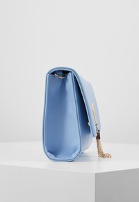 Ljusblå handväska med en slät yta, rektangulär form, gyllene kedja som accent och flikstängning. Har ett subtilt präglat mönster.