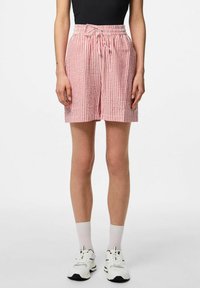 Červené a bílé pruhované šortky s elastickým pasem, stahovací šňůrkou a uvolněným střihem. Materiál vypadá jako lehký a prodyšný.