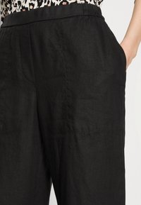 Zwarte linnen broek met zijzakken, met een relaxte pasvorm en een soepele textuur. Stikseldetails zijn zichtbaar bij de zakken.