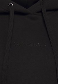 Schwarzer Baumwoll-Hoodie mit Kordelzug, versehen mit einem dezenten, geprägten Logo. Glatte Textur mit gerippten Akzenten an Kapuze und Bündchen.