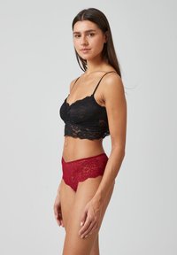 Zwarte kanten bralette met dunne bandjes, gecombineerd met rode kanten hipsteronderbroek, die ingewikkelde patronen en een gelaagde textuur toont.