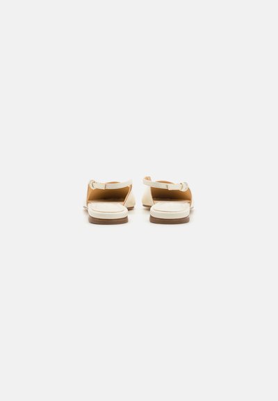 Sandali in pelle beige con suole bianche, dotati di cinturini alla caviglia regolabili e design flat. Texture liscia e stile minimalista elegante.