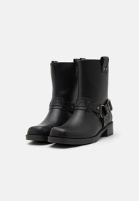 Botas negras hasta el tobillo de cuero suave, con una correa de hebilla lateral y acentos metálicos, y un tacón bajo tipo bloque.